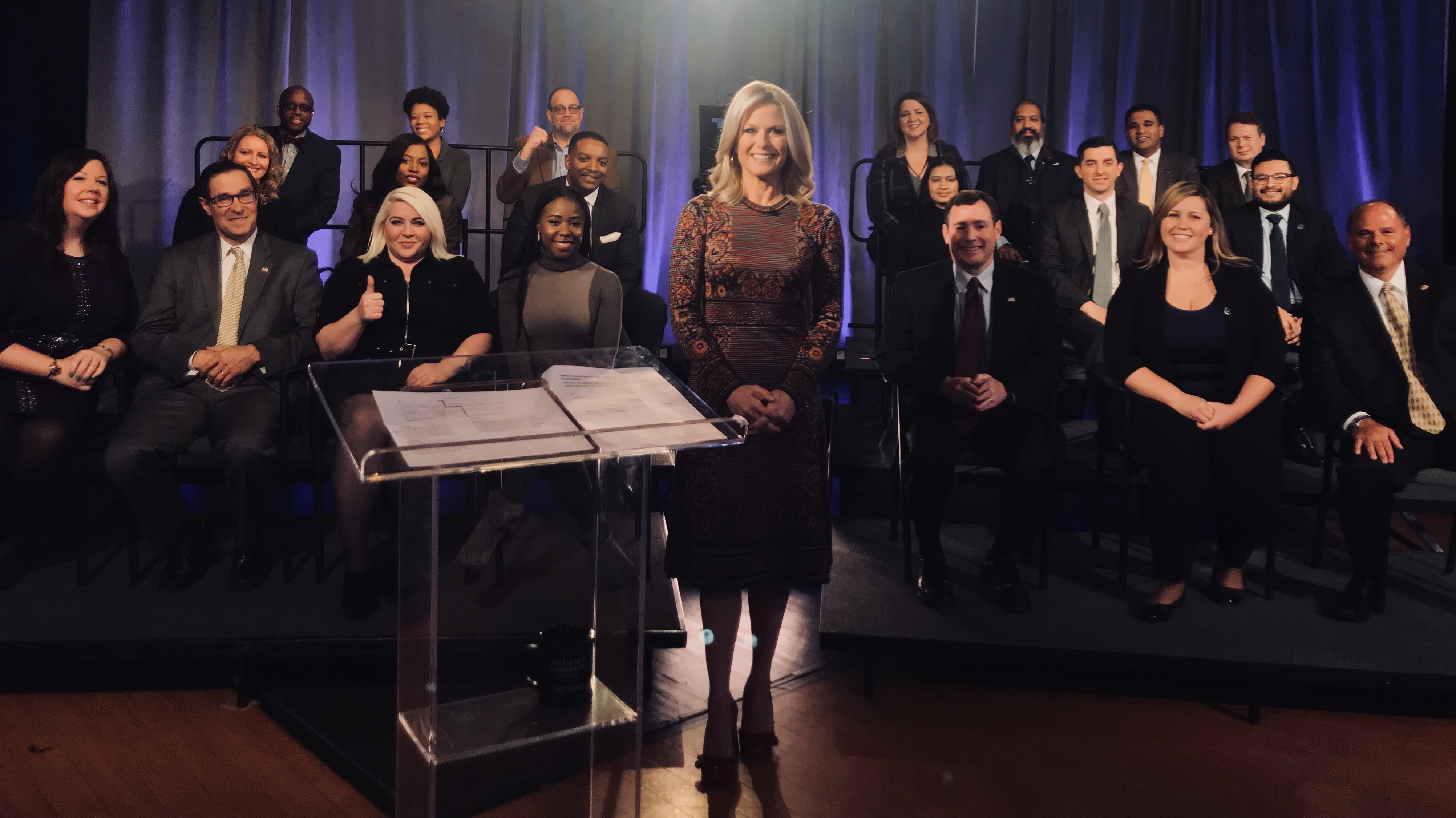 A woman standing in front of a podium with people behind her.