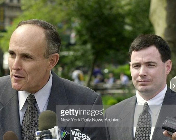 Two men in suits and ties are talking to reporters.